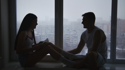 Family couple sitting on the windowsill, emotionally talking, arguing and gesticulating