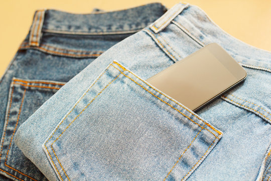 Picture of two jeans with mobile in pocket on craft wooden background