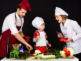 Concept of friendly family. Happy family in kitchen. Healthy food at home. Adorable kid in chef hat with parents. Cooking together. Preparation to dinner.