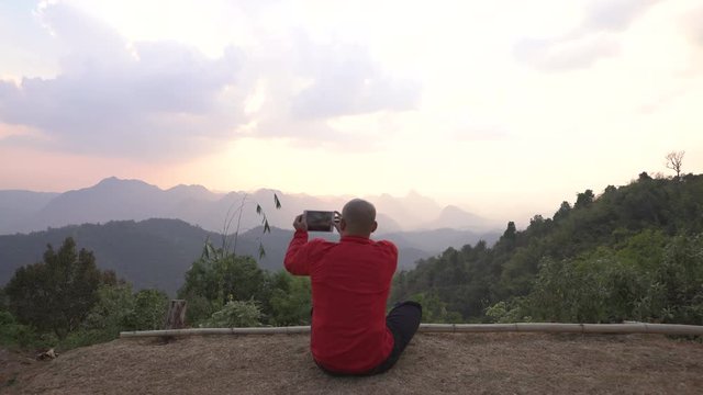 traveler take photo of hazy evening sky over mountain range landscape by digital tablet