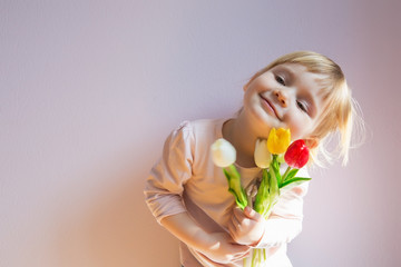 Sweet happy little blond-haired girl holding a bouquet of colorful tulips in her hands. Shot 3/4. Copy space.