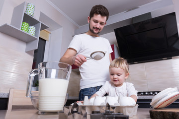 A tiny sweet girl with blond hair spends time with her dad, cooking in the kitchen. Preparations for the holidays. Baking.