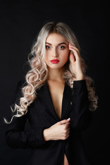 Sexy blonde with long curly hair poses in black jacket in a dark studio