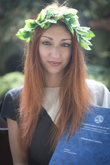 Portrait of a beautiful redhead girl holding her university final exam with a laurel wreath on her...