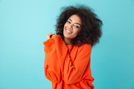 Colorful Portrait Of African American Woman In Red Shirt With Afro Hairstyle Looking On Camera With Smile Pressing Her Arms To Chest, Isolated Over Blue Background