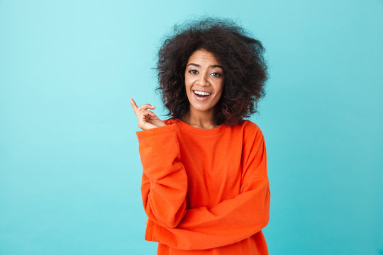 Content american woman in colorful shirt looking on camera and pointing finger up on copy space, isolated over blue background