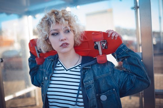 Woman holding skateboard at bus stop