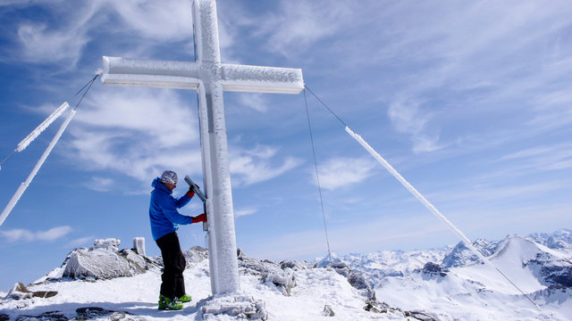 male backcountry skier at the summit cross of a high alpine peak on a beautiful winter day