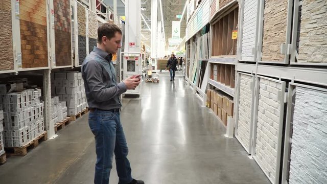 Guy at store of construction materials choosing wall covering for renovation 4k