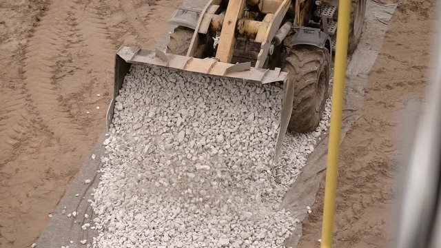 a close shot on a metal ladle, heavy machinery unloads small stones, pebbles on the road, in order then to put there asphalt