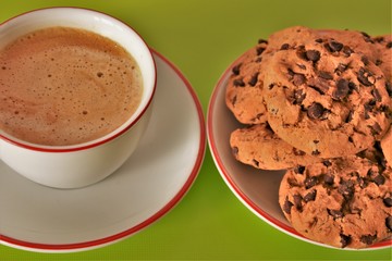 cup of coffee and cookies with chocolate on a white saucer on a green background