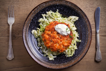 Salmon burger and cabbage salad in bowl on wooden table. Salmon fish cake and vegetables. overhead, horizontal