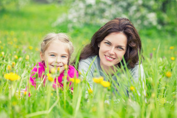 Mother and daughter lying on green summer grass with blooming yellow flowers