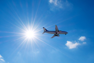 Passenger airplane flies in a blue sky with a bright sun.