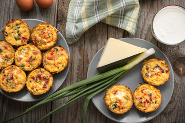 Muffins with scrambled eggs, cheese, bacon, potato and red pepper. Breakfast concept. Gray, rustic wooden background.