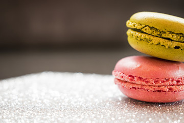 Pink strawberry and green pistachio macaroons on glitter silver base and dark background. Selective focus