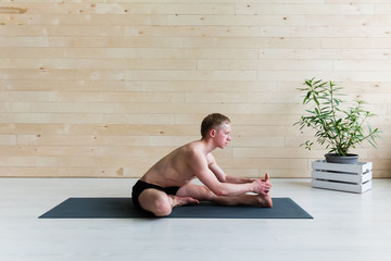 Fototapeta premium Sporty man doing Paschimottasana pose on yoga class