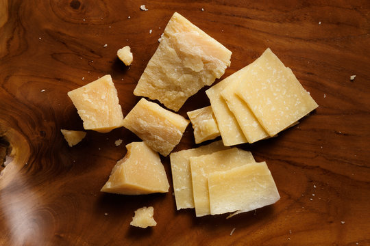 Pieces of parmesan or parmigiano reggiano cheese on a wooden board. Parmesan cheese uses in pasta, risotto and salads. Top view.