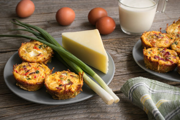Muffins with scrambled eggs, cheese, bacon, potato and red pepper. Breakfast concept. Gray, rustic wooden background.