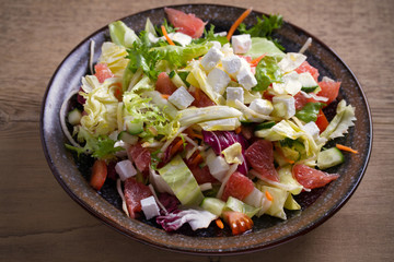 Healthy vegetarian food: citrus grapefruit, tomato, lettuce and cucumber salad with feta cheese in bowl on wooden table. horizontal