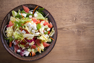 Healthy vegetarian food: citrus grapefruit, tomato, lettuce and cucumber salad with feta cheese in bowl on wooden table. overhead, horizontal