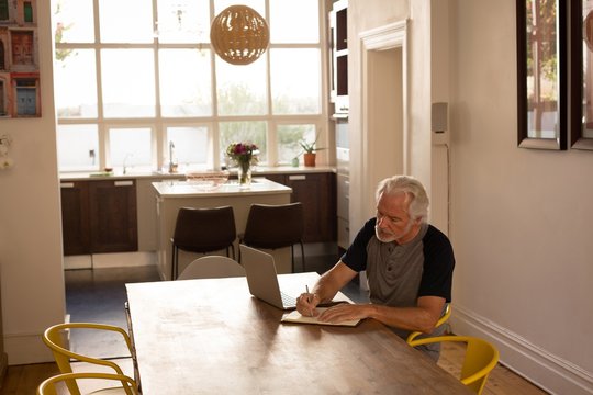 Senior man writing on a diary at home