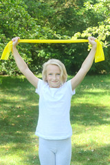 Obraz premium Beautiful school aged kid girl plays sports with a latex band outdoors in the park. Healthy lifestyle.