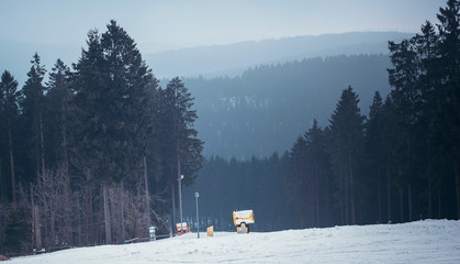 Ski slope with pine tree forest and ski cannon in mist. Winterberg, Germany.