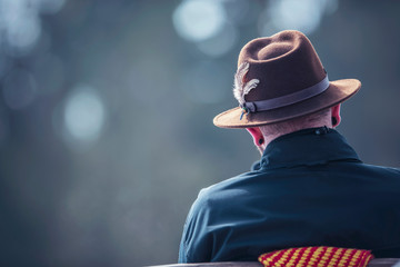 Man in brown fedora hat sitting outdoor on bench. Rear view. - obrazy, fototapety, plakaty