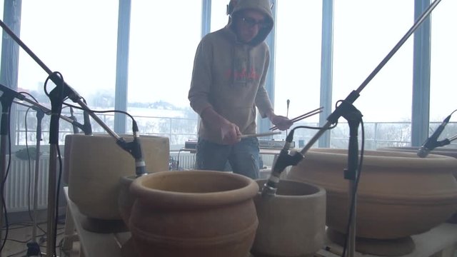 A man in a sweatshirt picks up drum sticks for playing on clay pots