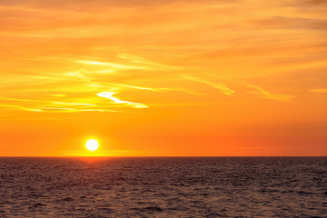 Beautiful round and bright sun setting against a vivid orange sky with high altitude tin clouds...