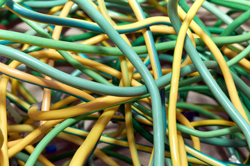 A bunch of electric yellow-green wires or cables crossed with each other. The wires are very complicated. Intertwining, chaos, mess. Tangle of patch cords.