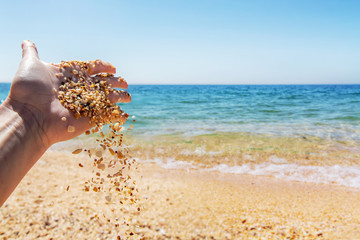 Woman hand scatter Seashells sand on the background of the sea