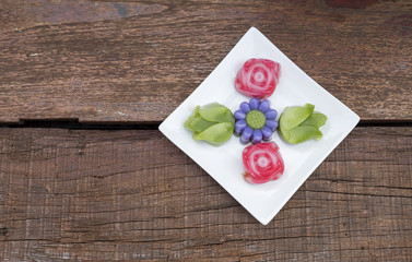 Colorful Thai layer cake design in different flower shape on white plate over old wooden table background