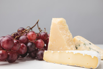 Closeup view of three types of cheese and grapes on gray