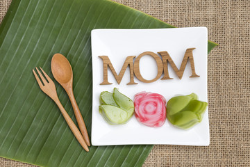 Mother's day concept idea, mom wooden text on white plate with mini Thai layer cake over green banana leaf and hessian fabric 