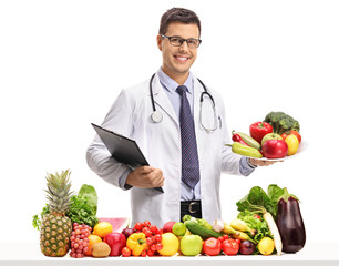 Doctor holding a clipboard and a plate behind a table with fruit and vegetables