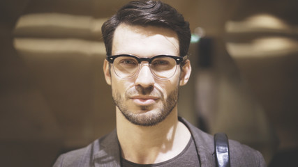 A closeup of a young confident bearded man wearing eyeglasses looking at the camera