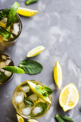 A few glass glasses with a cold tea with ice, mint and lemon on a gray concrete background. Summer cooling drink. Top view, flat lay