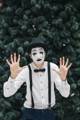 The man with the white face rested against the invisible glass. Clown mime. Mime. Play with the public. Show glass.