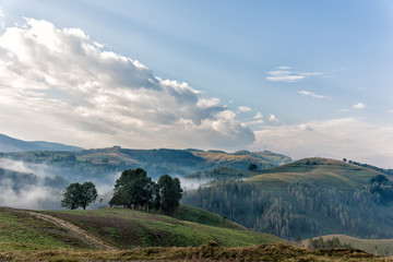 Beautiful mountain landscape of a foggy morning with and old house, trees and clouds, Dumesti, Salciua, Apuseni, Romania