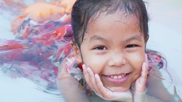 Portrait of happy asian child girl smiling and looking at camera while swimming in the rubber pool with fun in summer time with slow motion shot