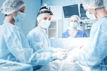 Emergency operation. Smart nice professional team of surgeons standing around the patient and...