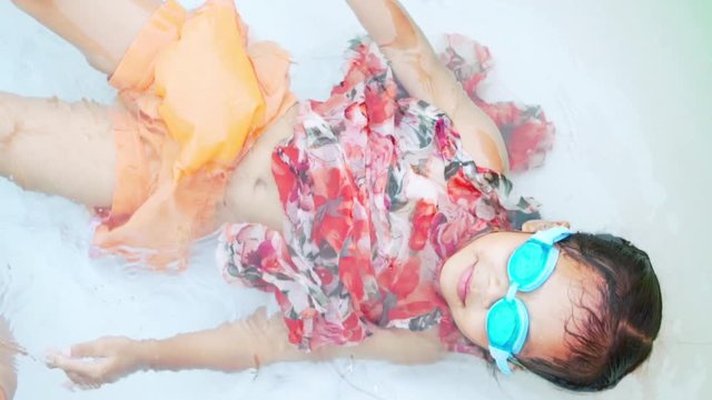 Cute asian child girl wearing swimming goggles swimming and lying down on the rubber pool with fun in summer time in slow motion shot