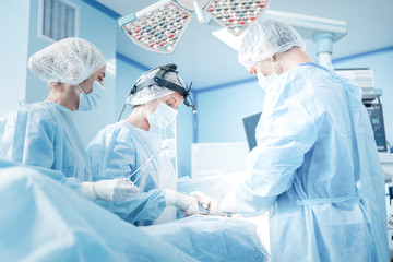 Urgent surgery. Professional smart intelligent surgeons standing near the patient and performing an...
