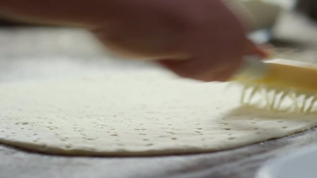 Close up hands of unrecognizable restaurant chef using dough roller when making pizza