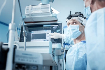Electronic equipment, Serious smart male surgeon pointing at the screen and looking at his colleague while checking his patients condition