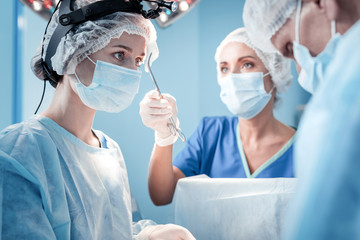 Team of professionals. Nice serious smart surgeon standing in the operation theater and looking at...