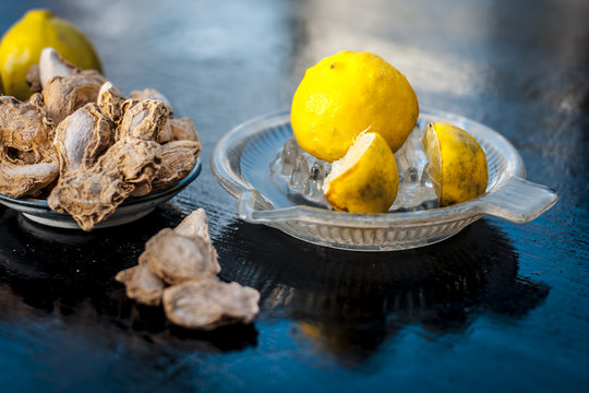 Raw fresh ripe lemons or Citrus &times; limon in a glass squeezer on black wooden surface in dark Gothic colors with ayurvedic herb dried ginger it helps in digestion,relief of cough, it is antifungal herb.