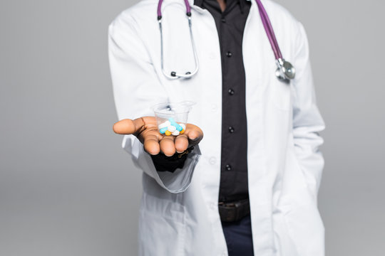 Afro american Doctor holding pills in hands isolated on gray background